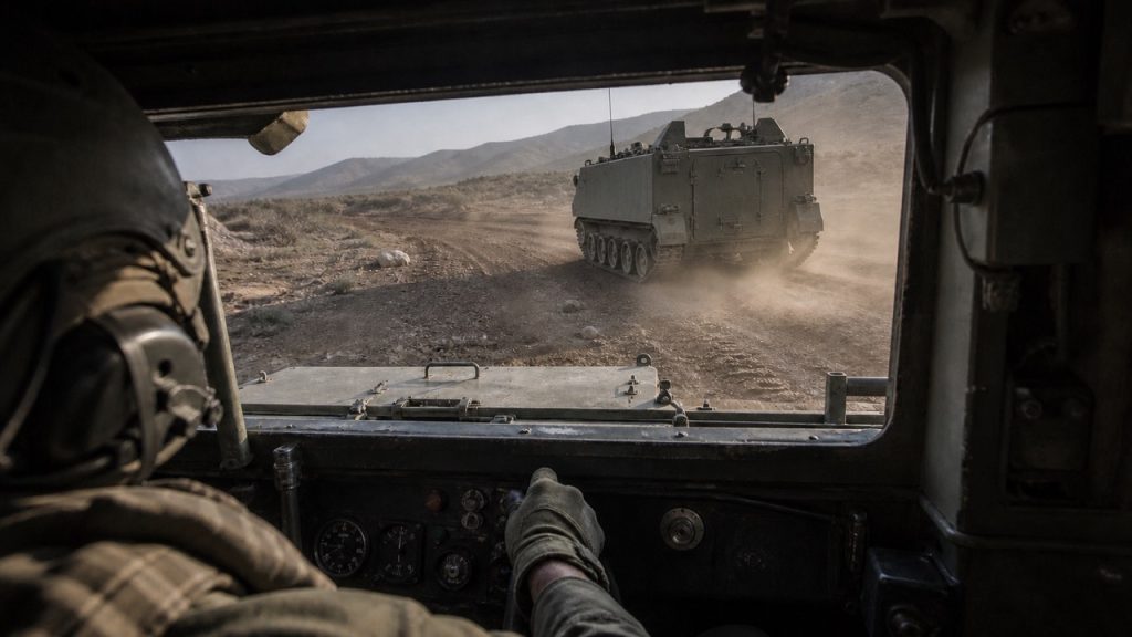 View from inside an M113 driver’s compartment following another M113 across a rugged and dusty training route.